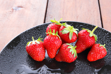 Strawberries on a black plate top view, red berries on a wooden background, fresh strawberries on dark wooden boards, vegetarian food