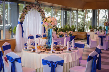 wedding flowers decoration and white chairs with blue bows in the restaurant