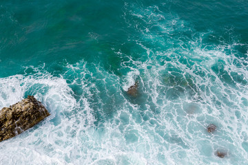 Big waves breaking on the shore. Waves and white foam. Coastal stones. View from above. The marine background is green