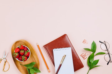 Business flatlay mockup with strawberries on a wooden tray, notebooks, glasses, ruscus branches and other accessories on pastel background with copyspace