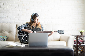 Fototapeta premium Woman recording a song on a guitar with her laptop