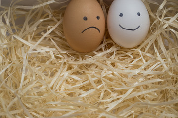 Chicken eggs with smileys sadness and smile lie on the hay