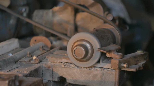 Old man sharpening the hoe. Work on a sharpening machine.