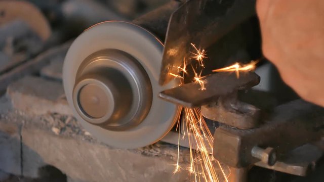 Old man sharpening the hoe. Work on a sharpening machine.