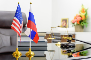 Flag of USA and Russia put together on a table with books, gavel and a balance scale of justice. A symbol of cooperation between Washington and Moscow i.e. military dialogue, diplomatic negotiation.