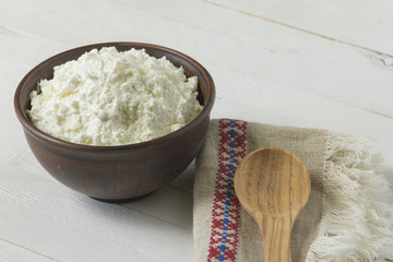Cottage cheese in a brown ceramic bowl with frozen raspberries and blackberries with authentic flax embroidered napkin and a wooden spoon on a white wooden background.  Close-up.