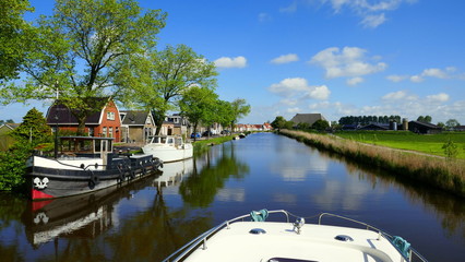 Hausboot fährt auf romantischem Kanal  entlang spiegelnden Häusern und Schiffen in Friesland