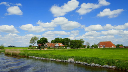 flache Landschaft in Friesland mit Kanal, grünen  Wiesen, Bauernhöfen und herrlichen Wolken