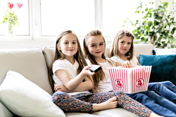 happy little girls watching comedy movie on tv and eating popcorn at home