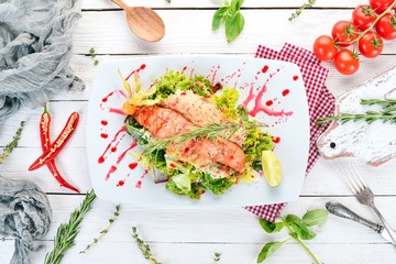 Salad with baked salmon and vegetables. On a wooden background. Top view. Copy space.