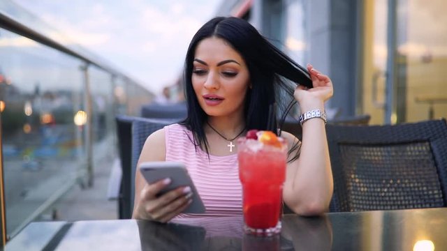 Woman drinking fresh cold cocktail looking down to smartphone