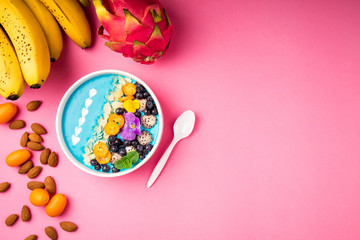 Smoothie bowl with fruits, berries, nuts and flowers on pink background. Tropical healthy smoothie dessert. Healthy breakfast, vegetarian food, lunch concept. Top view, flat lay