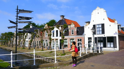 Fototapeta na wymiar junge Frau betrachtet Wegweiser des malerischen Dorfes Sloten in Friesland an sonnigem Tag
