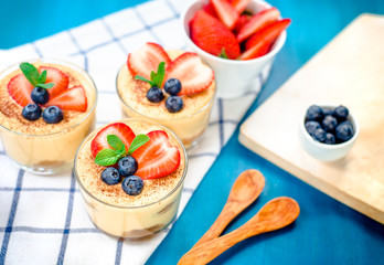 homemade, exquisite dessert tiramisu in glasses decorated with strawberry, blueberry, mint on blue wooden table