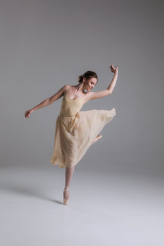 The tune of dancing feet! Full length photo of the young attractive enthusiastic ballerina dancing, while rising her leg on the beige background.