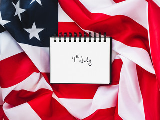 Fototapeta na wymiar Notepad with an inscription on July 4th against the background of the US flag. Preparation for the Independence Day. Top view, close-up. The concept of an independent, strong country and nation