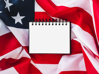 Fototapeta na wymiar US flag and blank page of the notebook for your inscriptions and congratulations on the national holidays of the USA. Top view, close-up. The concept of an independent, strong country and nation