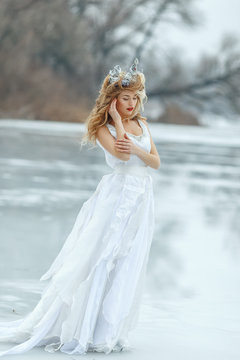 The Snow Queen. Young beautiful girl, blonde, in the image of a snow queen, on ice of a frozen river