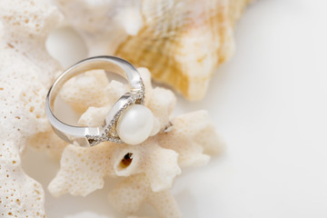 Silver ring with pearl and diamonds on coral against white background