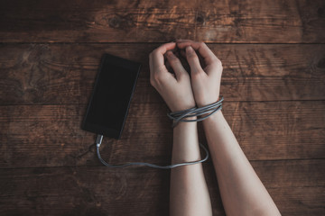 Cropped shot of woman with hands tied with smartphone wire, phone addiction concept