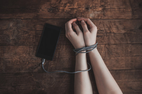 Cropped shot of woman with hands tied with smartphone wire, phone addiction concept