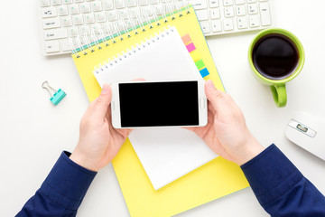 white desk, male hands, guy uses white smart phone, Notepad, office supplies,  white background with copy space, for advertisement, top view