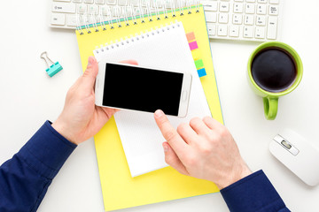 white desk, male hands, guy uses white smart phone, Notepad, office supplies,  white background with copy space, for advertisement, top view