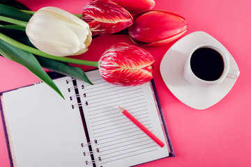 Notebook with a cup of esspresso coffee and fresh tulips on pink background
