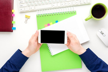 white desk, male hands, guy uses white smart phone, green Notepad, office supplies,  white background with copy space, for advertisement, top view