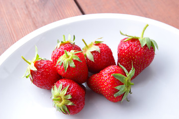 Strawberries on a white plate top view, red berries on a wooden background, fresh strawberries on dark wooden boards, vegetarian food