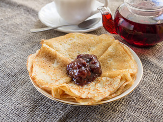 Pancakes on a plate with jam and a cup of tea