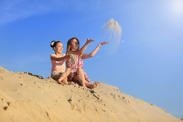 Dwie śliczne dziewczyny, siostry rzucają piaskiem na szczycie piaszczystej wydmy.