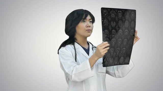 Female asian doctor wearing a white coat and stethoscope looking at x ray on white background