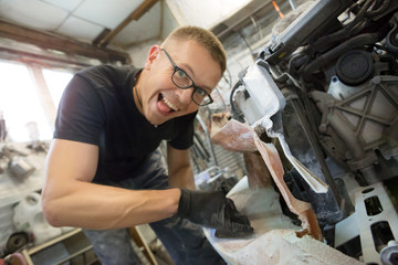 cute guy with glasses pulls the wing from the car with the help of sandpaper on the rough in the garage