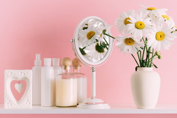 Obraz na płótnie Canvas Soft pink light bathroom decor for advertising, design, cover. Cosmetic set on light dressing table.Beautiful flowers in a vase on a pink wall background, mirror on a wooden shelf. mock up 