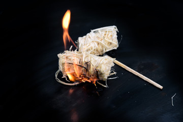burning wood wool barbecue lighter on a black metal bowl, copy space