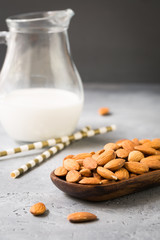 Glass jar of almond milk with almonds nuts in wooden bowl on dark grey background, copy space, healthy organic vegetarian drink, homemade diet natural dairy product