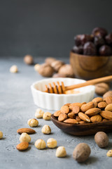 Assorted variety of nuts - walnuts, almonds and dry fruits, pumpkin seeds, chia, oats wooden spoon on dark grey background, healthy fitness superfood breakfast, copy space