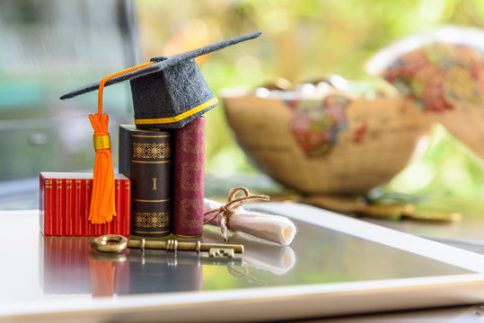 Graduate study abroad program for opening or expand world view concept : Graduation cap or hat, a key, world globe map, foreign text book on laptop, depicts achievement or success in online education