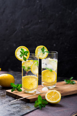 Lemon fruit lime slices caipirinha from Brazil, lemonade mint ice cubes in cold glasses on dark background, alcoholic mojito cockail ice tea green mint leaves, brown sugar spoon, copy space