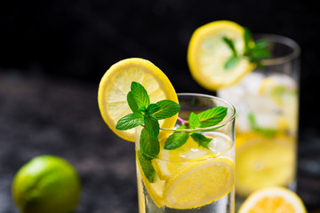 Lemon fruit lime slices caipirinha from Brazil, lemonade mint ice cubes in cold glasses on dark background, alcoholic mojito cockail ice tea green mint leaves, brown sugar spoon, copy space