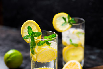 Lemon fruit lime slices caipirinha from Brazil, lemonade mint ice cubes in cold glasses on dark background, alcoholic mojito cockail ice tea green mint leaves, brown sugar spoon, copy space