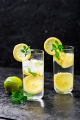 Lemon fruit lime slices caipirinha from Brazil, lemonade mint ice cubes in cold glasses on dark background, alcoholic mojito cockail ice tea green mint leaves, brown sugar spoon, copy space