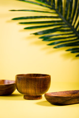 Wooden bamboo asian spa bowls on summer tropic yellow background with palm tree green leaf, china and japan tradition bath therapy treatment bowls for salt and oils, relaxation set up arrangement  