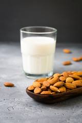 Glass jar of almond milk with almonds nuts in wooden bowl on dark grey background, copy space, healthy organic vegetarian drink, homemade diet natural dairy product