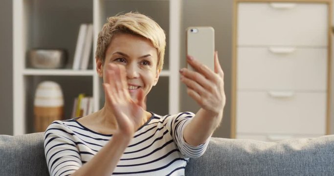 Close up of the Caucasian pretty woman with short hair sitting on the sofa at home and having videochat on the smartphone. Indoor
