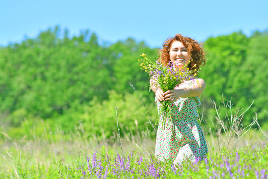 Young and happy redhead girl with flowers on a forest meadow