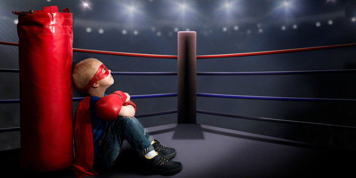 A child in a superhero costume sits in the ring and dreams of boxing victories.