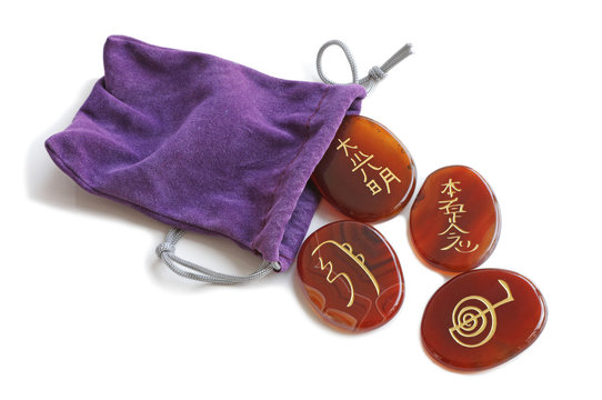 Reiki Stones and Purple Velvet carrying bag - four carnelian stones gold etched with the four main Reiki Symbols isolated on a white background 
