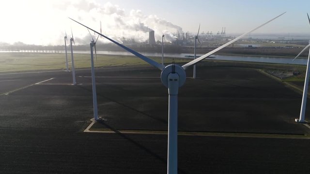 Aerial wind turbine park nuclear power plant and industry in background showing the cooling tower rejecting waste heat to the atmosphere forming thick layers of industrial exhaust 4k high resolution